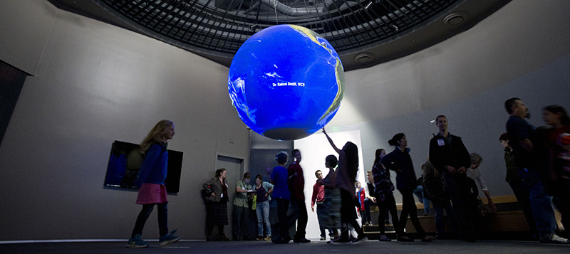 Child reaches up to touch a blue globe, the Science on a Sphere exhibit.